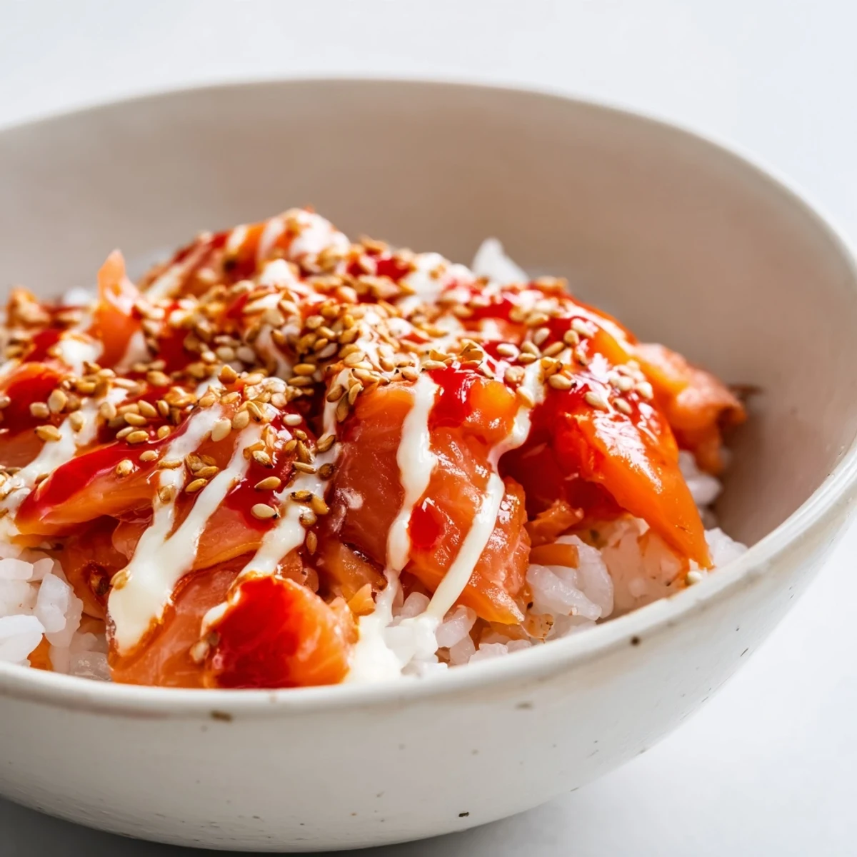 A close-up of Emily Mariko's salmon rice bowl with flaked fish, creamy avocado slices, spicy mayo drizzle, and sesame seeds over warm rice.
