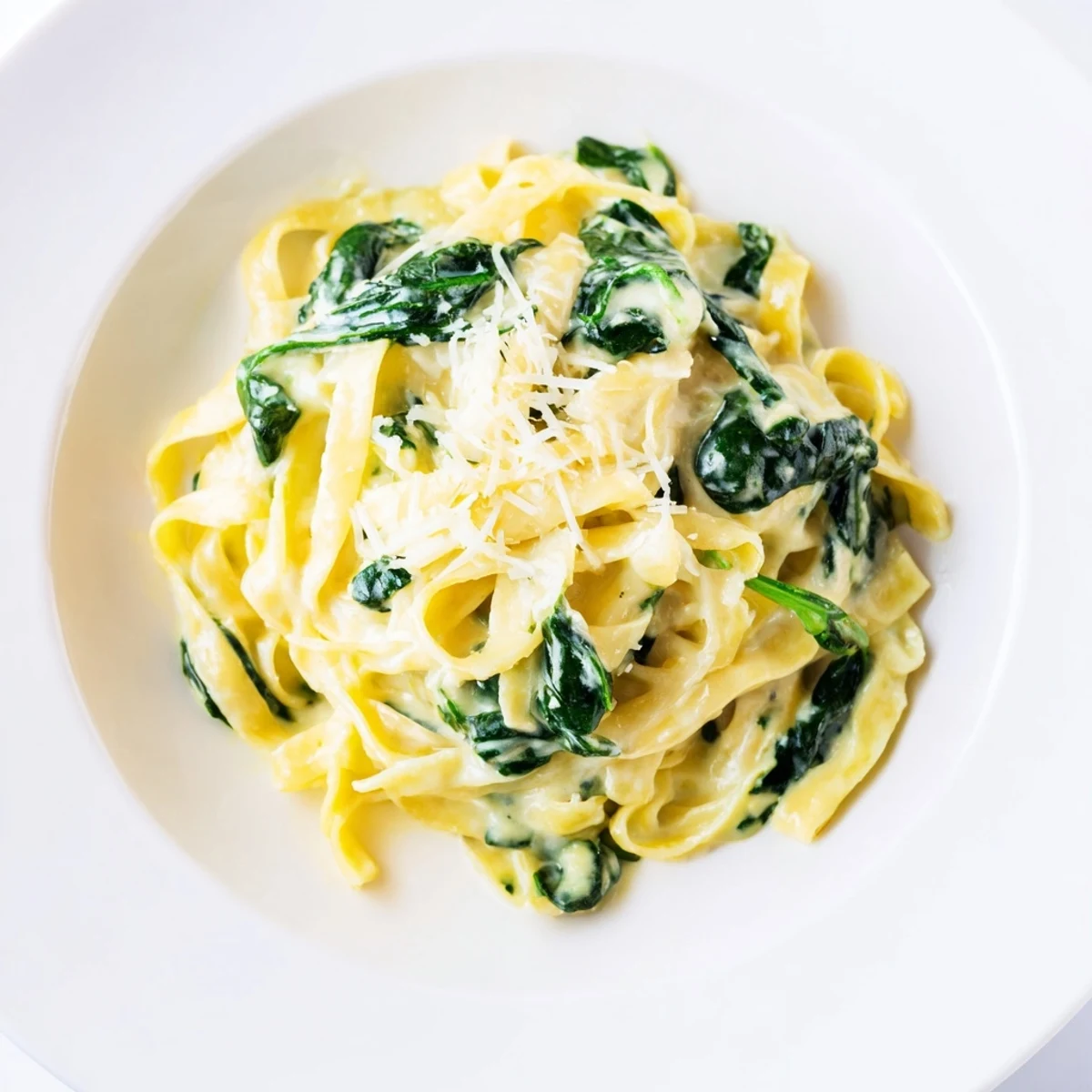 A bowl of creamy garlic spinach pasta with wilted greens, paired with a glass of white wine for dinner.