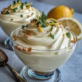 Lemon mousse cups with shortbread cookies in a glass, garnished with fresh berries and mint leaves.