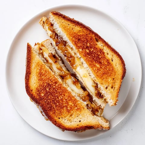 Golden-brown sourdough grilled cheese layered with sweet, jammy caramelized onions and melted sharp white cheddar on a plate.