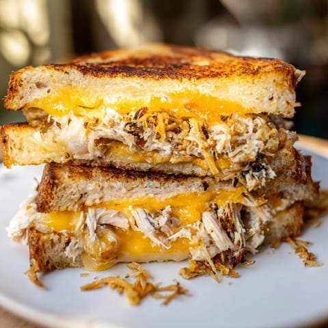A close-up of a beautifully melted Crispy Shallot Chicken Grilled Cheese, ready to be sliced and enjoyed.