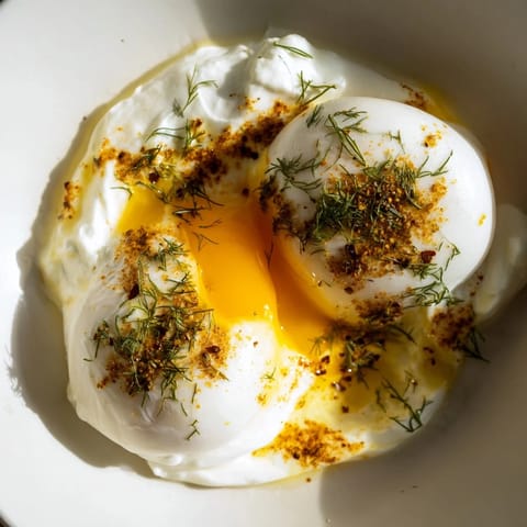 A close-up of a Cilbir dish: creamy yogurt, sunny eggs, and a drizzle of rich brown butter.