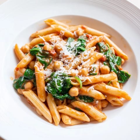 A close-up view of Creamy Tuscan Chickpea Pasta, highlighting the rich, creamy tomato sauce coating the noodles, with chickpeas and wilted spinach visible.