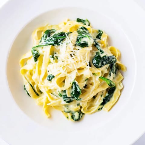 A bowl of creamy garlic spinach pasta with wilted greens, paired with a glass of white wine for dinner.