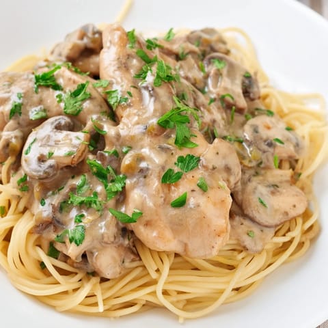 Tender spaghettini pasta with creamy mushroom sauce and golden chicken, garnished with fresh parsley and grated Parmesan cheese.