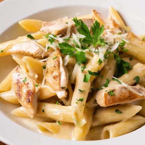 Golden-brown roasted chicken slices and al dente penne coated in a creamy, roasted garlic sauce, garnished with fresh parsley and Parmesan.