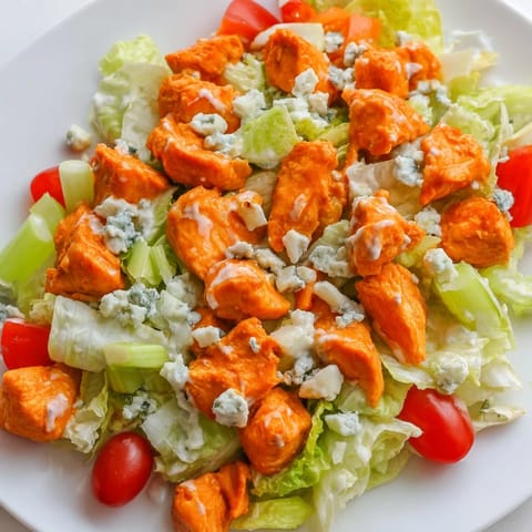 Tossed Buffalo Chicken Chopped Salad garnished with juicy cherry tomatoes, shredded carrots, and a drizzle of creamy dressing.