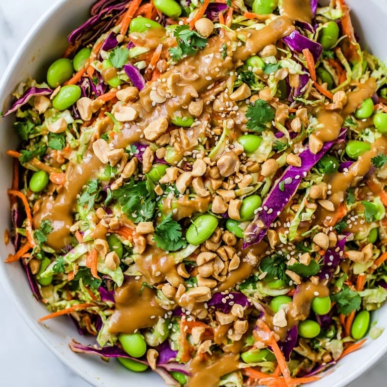 Serving suggestion for Crunchy Thai Peanut Salad: a colorful mix of shredded cabbage, carrots, edamame, and bell pepper, with lime wedges on the side for squeezing.