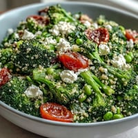 Vibrant quinoa grain bowl with broccoli, peas, and crumbled feta, drizzled with lemon Dijon dressing for a fresh, satisfying vegetarian meal.  